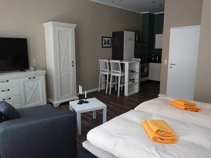 A hotel room with a bed, a TV, a wardrobe, a small table, and a kitchenette in the background. - Ferienwohnung Café Flair (Görlitz)