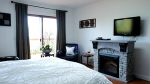 A hotel room with a bed, a fireplace, a television, and a view of the outdoors. - Entire room. Ocean,mountain view, hot tub,garden,deck,next to Mount Maxwell park (Salt Spring Island)