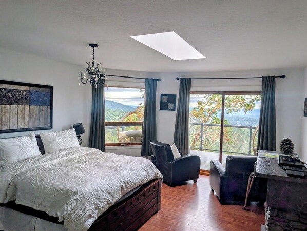A bedroom with a large bed, a desk, and a chair. There is a skylight above the bed and a view of the outdoors. - Entire room. Ocean,mountain view, hot tub,garden,deck,next to Mount Maxwell park (Salt Spring Island)
