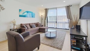 Ein modernes Wohnzimmer mit einem Ecksofa, einem Couchtisch und einem Flachbildfernseher auf einem TV-Möbel.