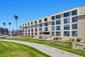 A multi-story hotel with a flat facade, large windows, and a parking area with cars. - New Photos! Direct beach access+pool+parking (San Diego)