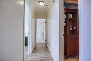 A narrow hallway with wooden flooring and white walls, leading to a door at the end. - New Photos! Direct beach access+pool+parking (San Diego)