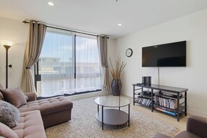 A modern living room with a sofa, a coffee table, a bookshelf, and a TV mounted on the wall.