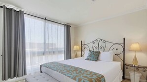 Ein Hotelzimmer mit Bett, zwei Nachttischlampen, einem Fenster mit Vorhängen und einer kleinen Bank.