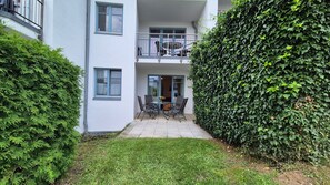 Une cour avec une table et des chaises, entourée d’une haie et bordée d’un immeuble doté de balcons.