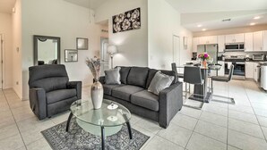 Ein modernes Wohnzimmer mit einem grauen Sofa, einem Glastisch und einem Essbereich mit kleinem Tisch und Stühlen.