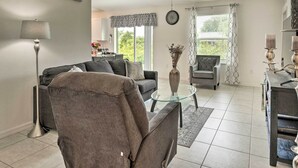 Ein modernes Wohnzimmer mit Sofa, Sessel und Couchtisch. Durch das Fenster ist ein Essbereich mit Tisch und Stühlen zu sehen.