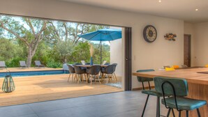 A modern dining area with a wooden table and chairs, a blue umbrella, and a view of a swimming pool and trees. - Villa Pienezza 8p 4 bedrooms very quiet Pinarellu 5min from beaches Heated swimming pool (Pinarellu)