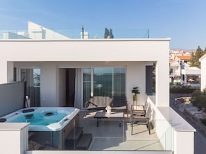 A modern balcony with a hot tub, outdoor seating, and a glass door leading to an interior space.