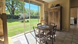 A dining area with a table and chairs, a sliding glass door to a garden, and a wooden cabinet. - Charming Dordogne house with fireplace and enclosed garden (Lalinde)