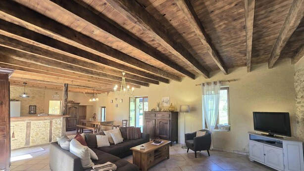 A rustic interior with exposed wooden beams, a sofa, a television, and a dining area. - Charming Dordogne house with fireplace and enclosed garden (Lalinde)
