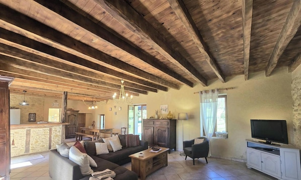 A rustic interior with exposed wooden beams, a sofa, a television, and a dining area.