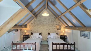 A bedroom with two beds, a stone wall, wooden beams, and a hanging light fixture. - Charming Dordogne house with fireplace and enclosed garden (Lalinde)
