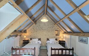 A bedroom with two beds, a stone wall, wooden beams, and a hanging light fixture.