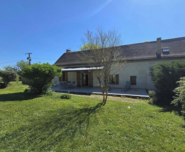 Une maison à deux étages avec un porche, un petit arbre et une cour gazonnée.