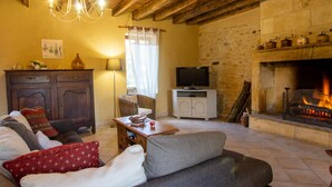 A cozy living room with a fireplace, a television, and a stone wall. - Charming Dordogne house with fireplace and enclosed garden (Lalinde)