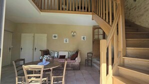A dining area with a wooden table, chairs, a sofa, and a staircase. - Charming Dordogne house with fireplace and enclosed garden (Lalinde)