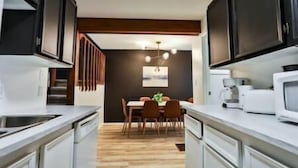Una cocina moderna con encimeras blancas, armarios oscuros y una zona de comedor de madera.
