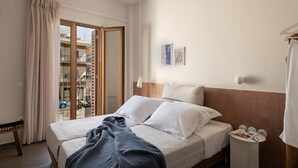 A hotel room with a bed, a bedside table with a lamp, a window with curtains, and a view of the outside balcony. - Lofos Casteli Sunlight (Chania)