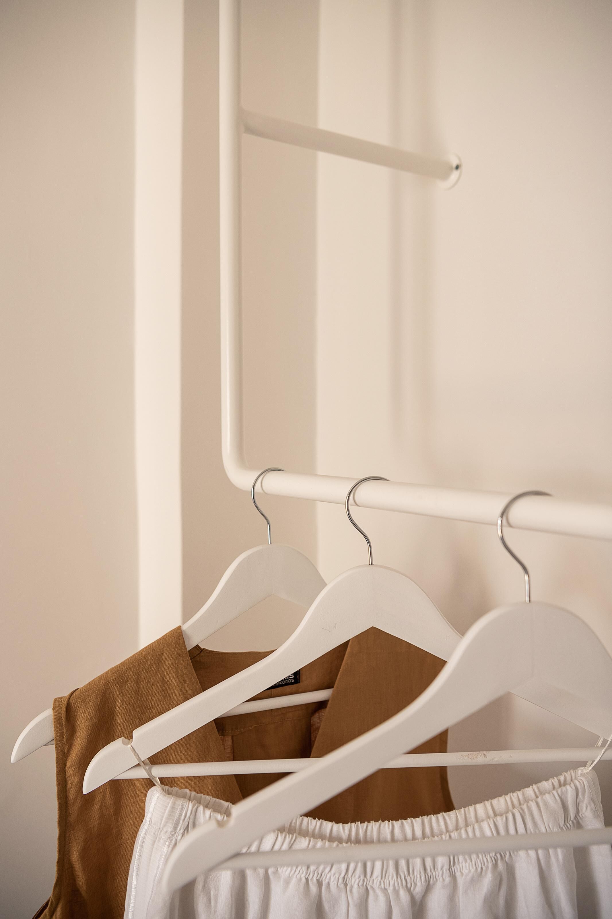 A white metal rack with two white hangers, one holding a brown garment and the other a white garment.