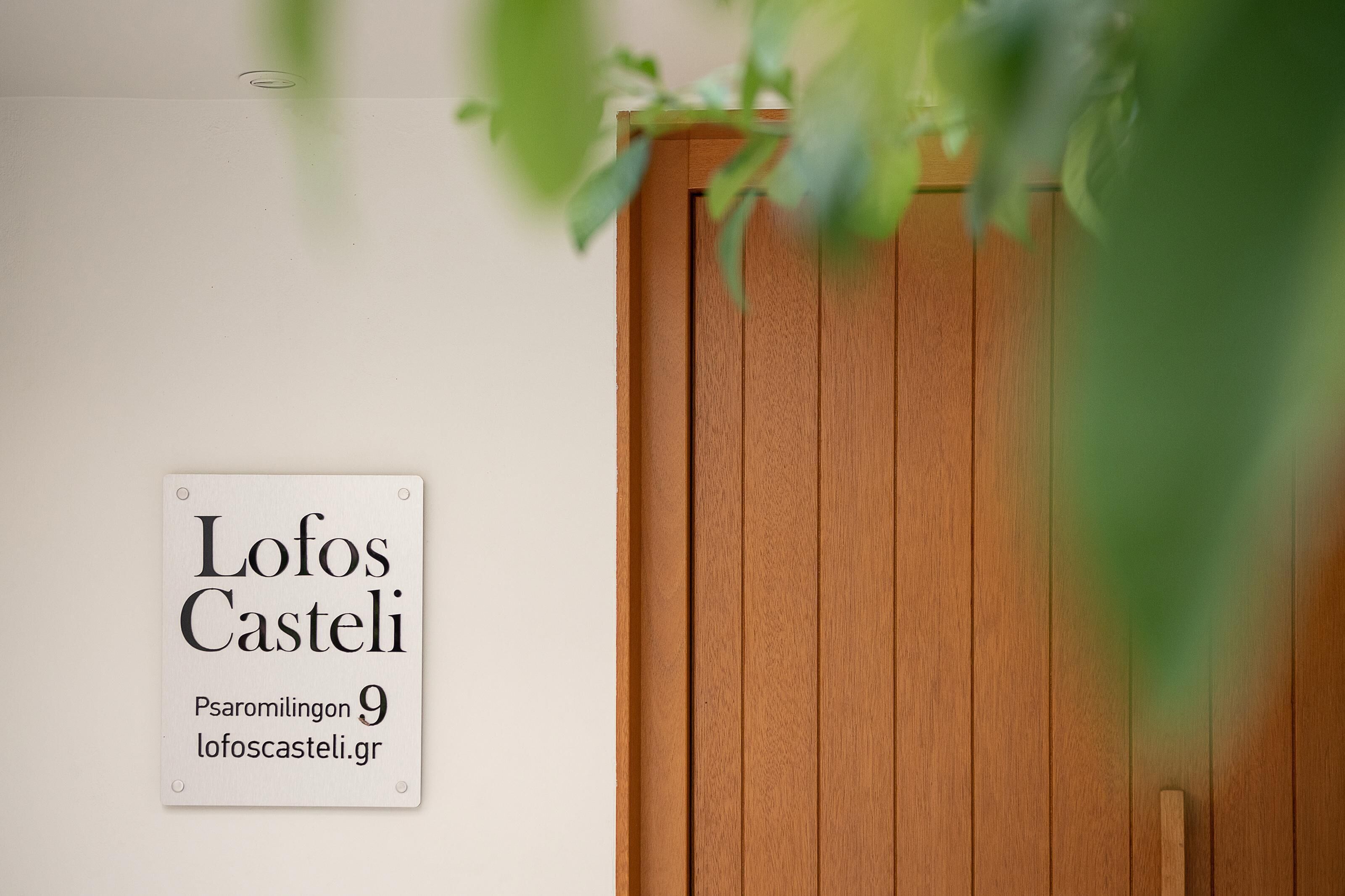 Un letrero con el texto 'Lofos Casteli' y una puerta de madera.