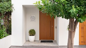 A modern building entrance with a wooden door, a sign reading "Lofo Castle," and a potted plant. - Lofos Casteli Sunlight (Chania)
