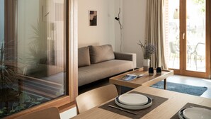 A modern living room with a sofa, a dining table set for two, and a large window with a view of the outdoors. - Lofos Casteli Sunlight (Chania)