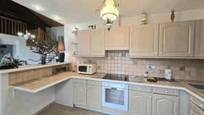 A kitchen with light-colored cabinets, a microwave, an oven, and a hanging light fixture.