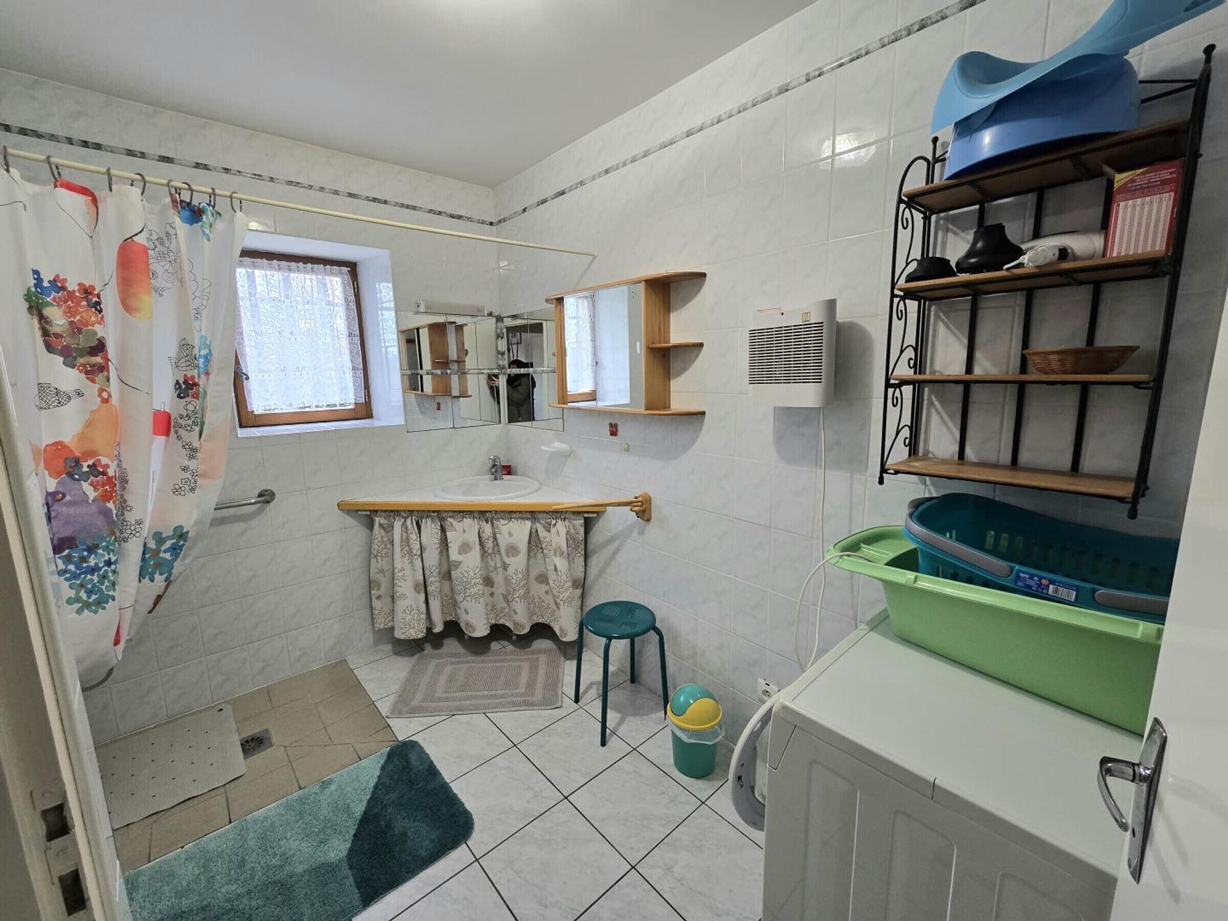 Une petite salle de bain équipée d’un rideau de douche, d’un lavabo, d’un miroir, d’un radiateur et d’une étagère contenant des articles de toilette.