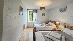 A bedroom with two beds, a window with curtains, a ceiling light, and framed pictures on the walls.