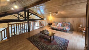 A spacious loft with a high ceiling, wooden beams, a cozy seating area with a colorful sofa, a small table, and a rug.