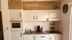 A compact kitchen with white cabinetry, a built-in oven, a coffee maker, and a dishwasher. - Studio cabin with sea view and garage in Fort-Mahon plage (Fort-Mahon-Plage)