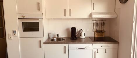 A compact kitchen with white cabinetry, a built-in oven, a coffee maker, and a dishwasher.
