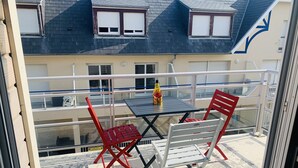 A balcony with a table and two chairs, a bottle of water, and a building with multiple windows in the background. - Studio cabin with sea view and garage in Fort-Mahon plage (Fort-Mahon-Plage)