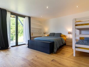 Quarto com cama, mesa de cabeceira, abajur, beliche e porta de vidro deslizante que dá para uma varanda.