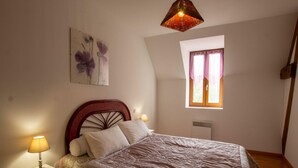 Een slaapkamer met een bed, een nachtkastje, een wandlamp, een raam met gordijnen en een schilderij aan de muur.