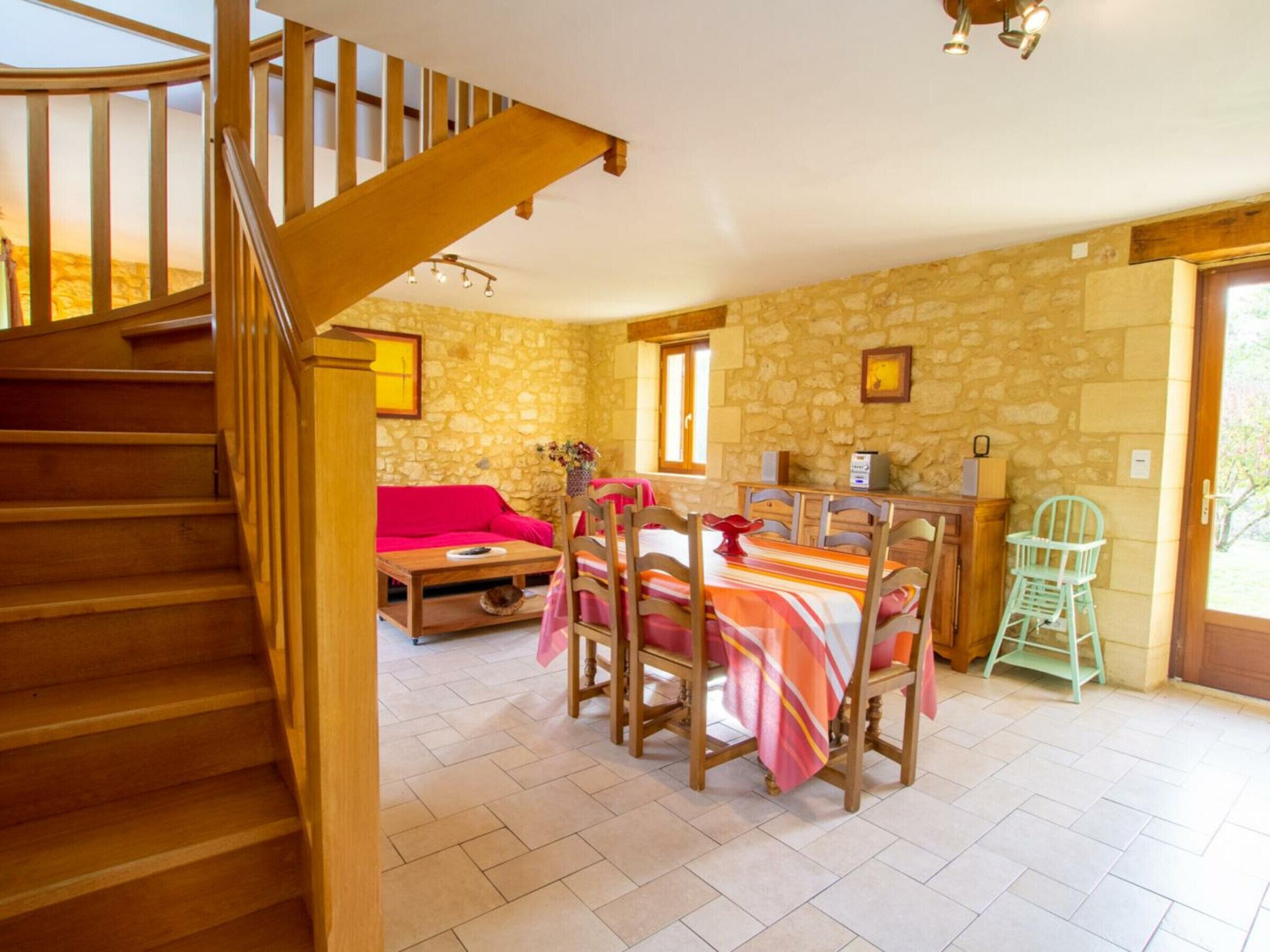 A wooden staircase leading to a room with a stone wall, a dining table with chairs, a red sofa, and a small table with a vase.