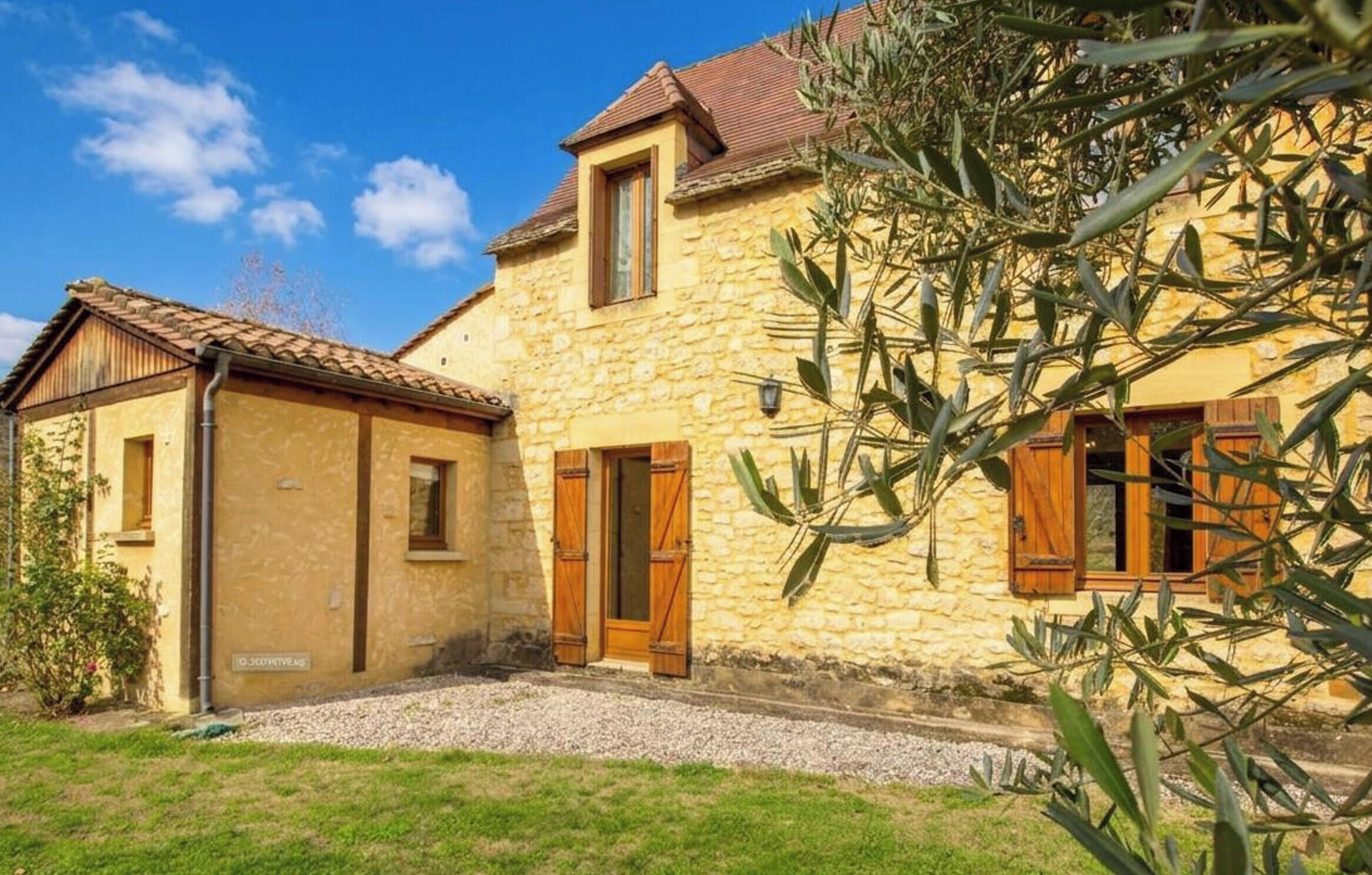 Un bâtiment en pierre avec un toit en tuiles, des volets en bois et une allée gravillonnée.
