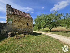 A stone building with a tiled roof, a sign indicating it is a GITE, and a dirt path leading to it.