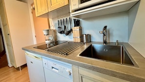 Een kleine keuken met een vaatwasser, een koffiezetapparaat, een magnetron en een spoelbak.