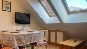 Een eethoek met een tafel gedekt voor twee personen, een televisie aan de wand en een dakraam erboven.