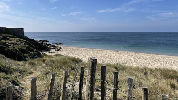 A beach with a wooden fence in the foreground, a stone wall on the left, and a clear blue sky. - Bel Appartement Proche de la Plage (56640 - ARZON)