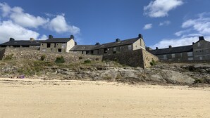 A coastal stone building with multiple rooms, a sandy beach in the foreground, and a clear blue sky. - Bel Appartement Proche de la Plage (56640 - ARZON)