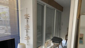 A modern living room with a TV, remote, and lamp on a white console. A patterned rug and a bench are visible. - Bel Appartement Proche de la Plage (56640 - ARZON)