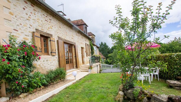 A stone building with a garden, a small outdoor seating area, and a stone wall.