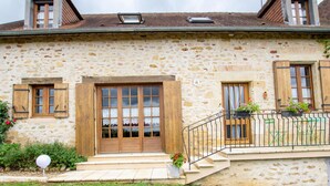 A stone building with a wooden door, windows, and a small balcony with potted plants.