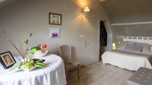 A bedroom with two beds, a chair, a table with a floral arrangement, and artwork on the walls.