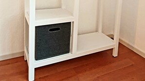 A white, three-tiered, open shelving unit with a wooden hanger rack on the right side. - Lichtdurchflutetes Apartment im Herzen der City (Bielefeld)