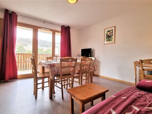 Uma sala de jantar com mesa posta para quatro pessoas, cadeiras de madeira, uma mesinha e um sofá.
