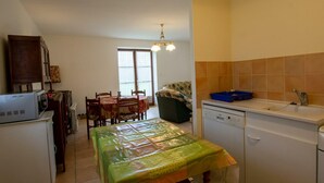 A compact kitchen with a dining table, a refrigerator, a dishwasher, and a window with blinds. - Charming Quiet House Near Sarlat with Fireplace and Terrace (Tursac)